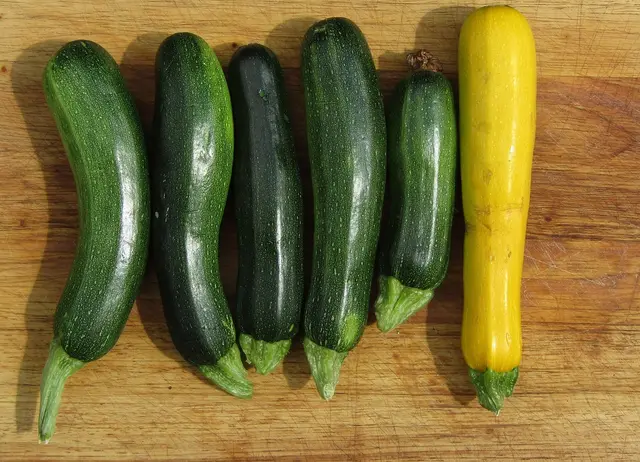 Five green courgettes and one yellow courgette on a wooden board